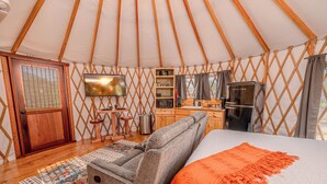 En hyggelig yurt-indretning med seng, siddeplads, køkken og et fjernsyn.