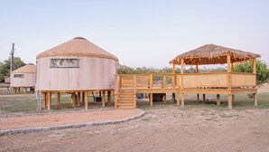En yurt med en træterrasse og en overdækket pavillon med stråtækt tag.