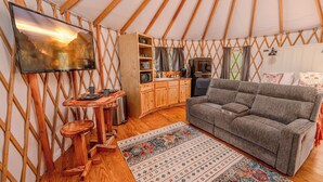 Indretningen i en yurts hyggelige rum med sofa, træskabe, fjernsyn og et mønstret tæppe.