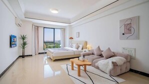 Een moderne woonkamer met een bank, een bed, een salontafel en een groot raam.