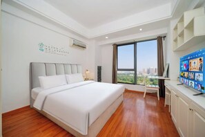 Ein Hotelzimmer mit einem großen Bett, einem Schreibtisch mit Computer, einem Fernseher und einem Fenster mit Blick auf die Stadt.