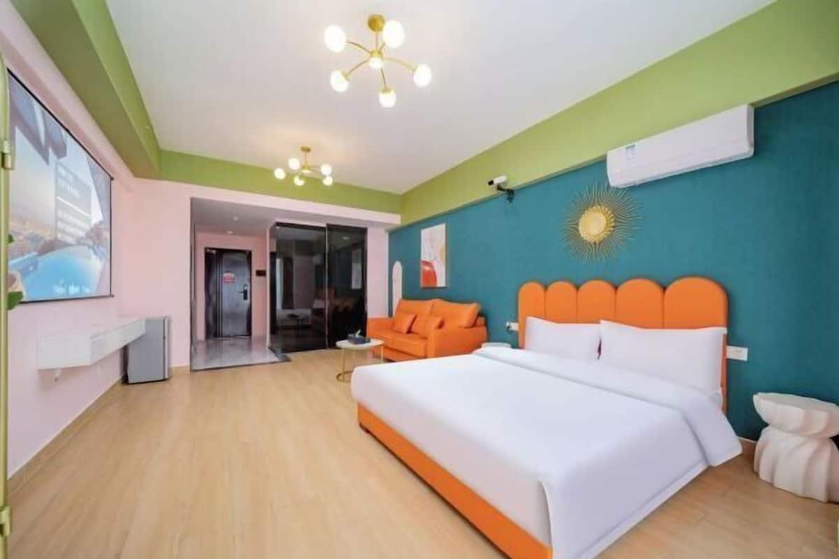 Ein Hotelzimmer mit einem Bett, einer orangefarbenen Kopfteil, einer weißen Wand, einer Deckenleuchte und einer Tür zu einem weiteren Raum.