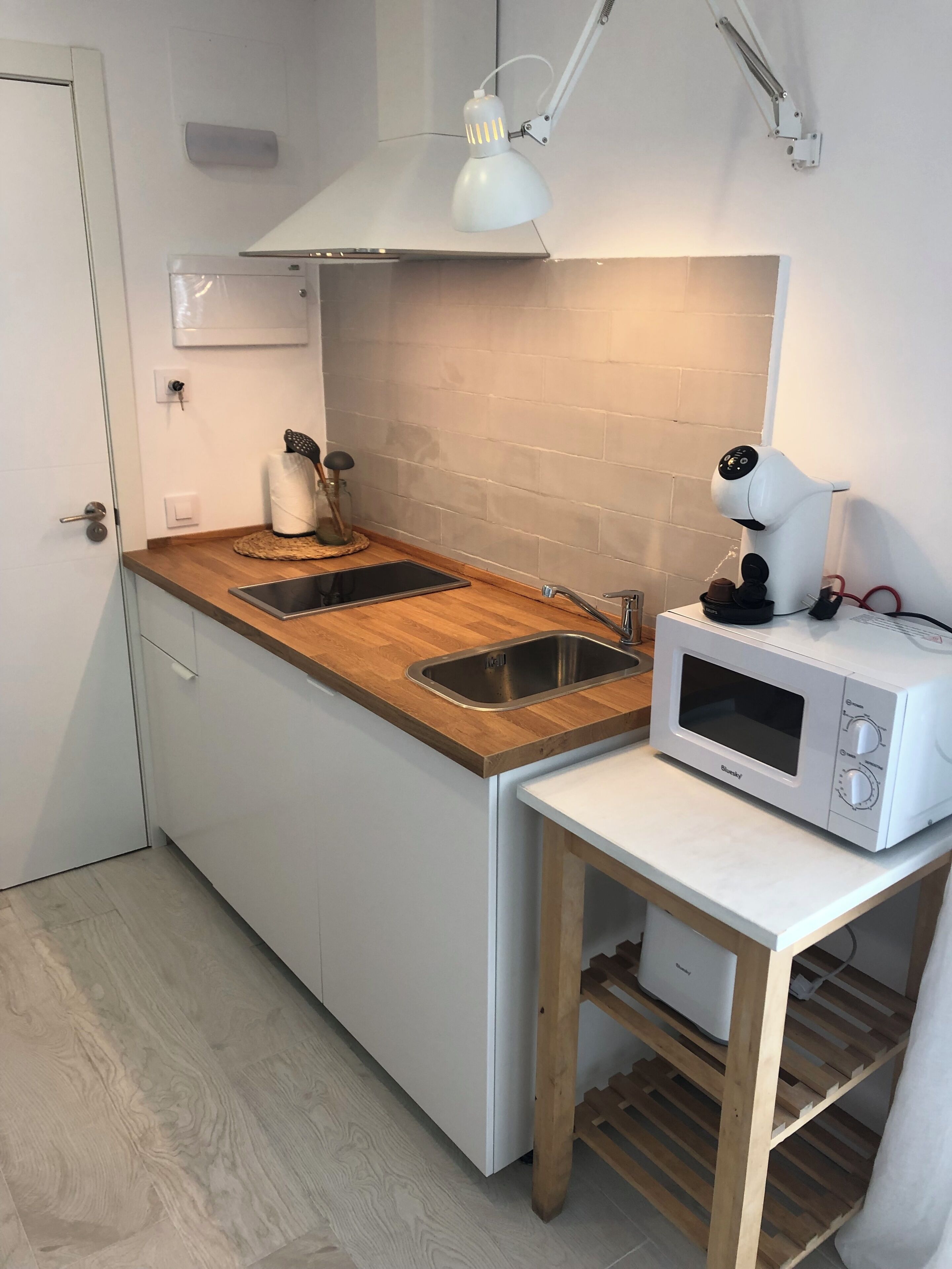 Une cuisine compacte dotée d’un plan de travail en bois, d’un évier à deux bacs, d’un four à micro-ondes et d’une petite table avec une lampe.