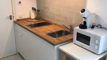 Une cuisine compacte dotée d’un plan de travail en bois, d’un évier à deux bacs, d’un four à micro-ondes et d’une petite table avec une lampe.