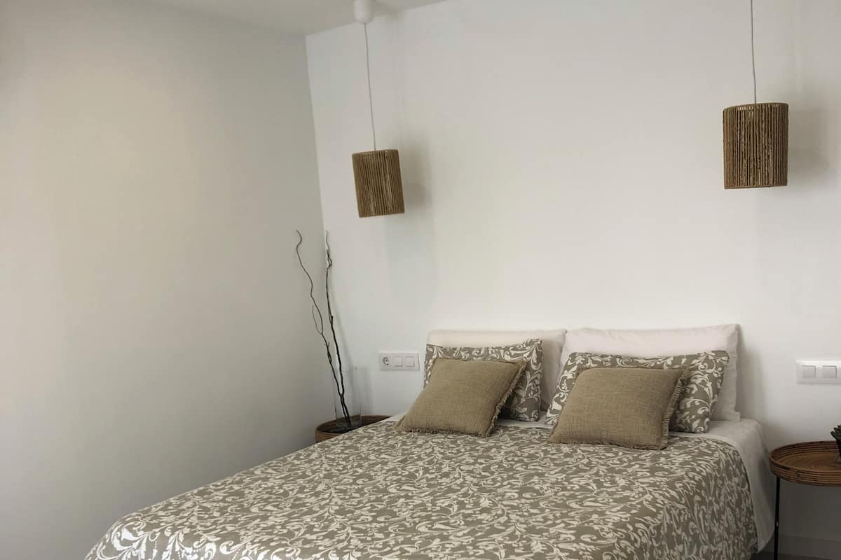 A neatly made bed with a patterned bedspread, a bedside table with a lamp, and a woven rug on the floor.