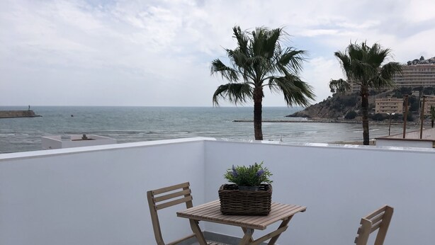 A balcony with a table and chairs, a patterned rug, and a view of the sea and palm trees. - Estudios Peñiscola  (Peñíscola)