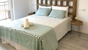 A bedroom with a wooden headboard, a bed with a green and white bedspread, a small round side table with a vase, and a balcony door. - Estudios Peñiscola  (Peñíscola)