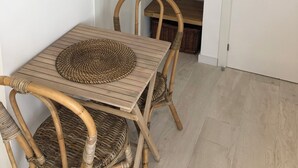 A small dining area with a wooden table and chairs, a woven placemat, and a shelf with baskets and hangers. - Estudios Peñiscola  (Peñíscola)
