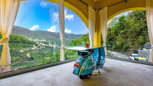 Une pièce avec un scooter bleu, de grandes fenêtres avec des rideaux et une vue sur un paysage verdoyant.