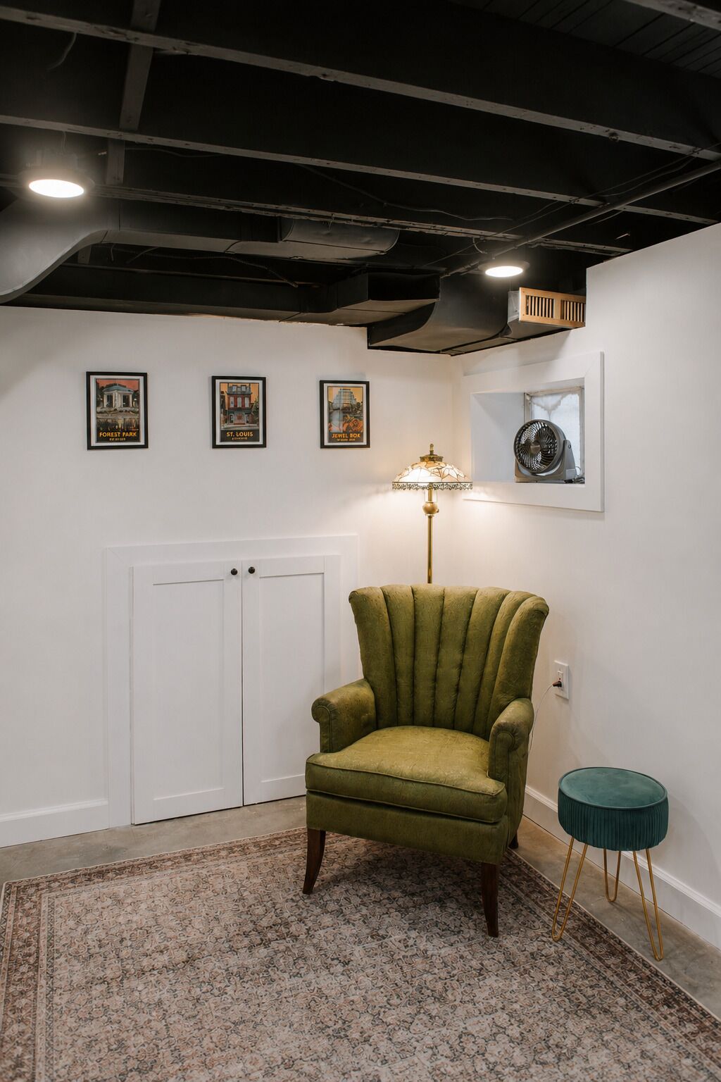 A room with a green armchair, a patterned rug, a standing lamp, and framed pictures on the wall.