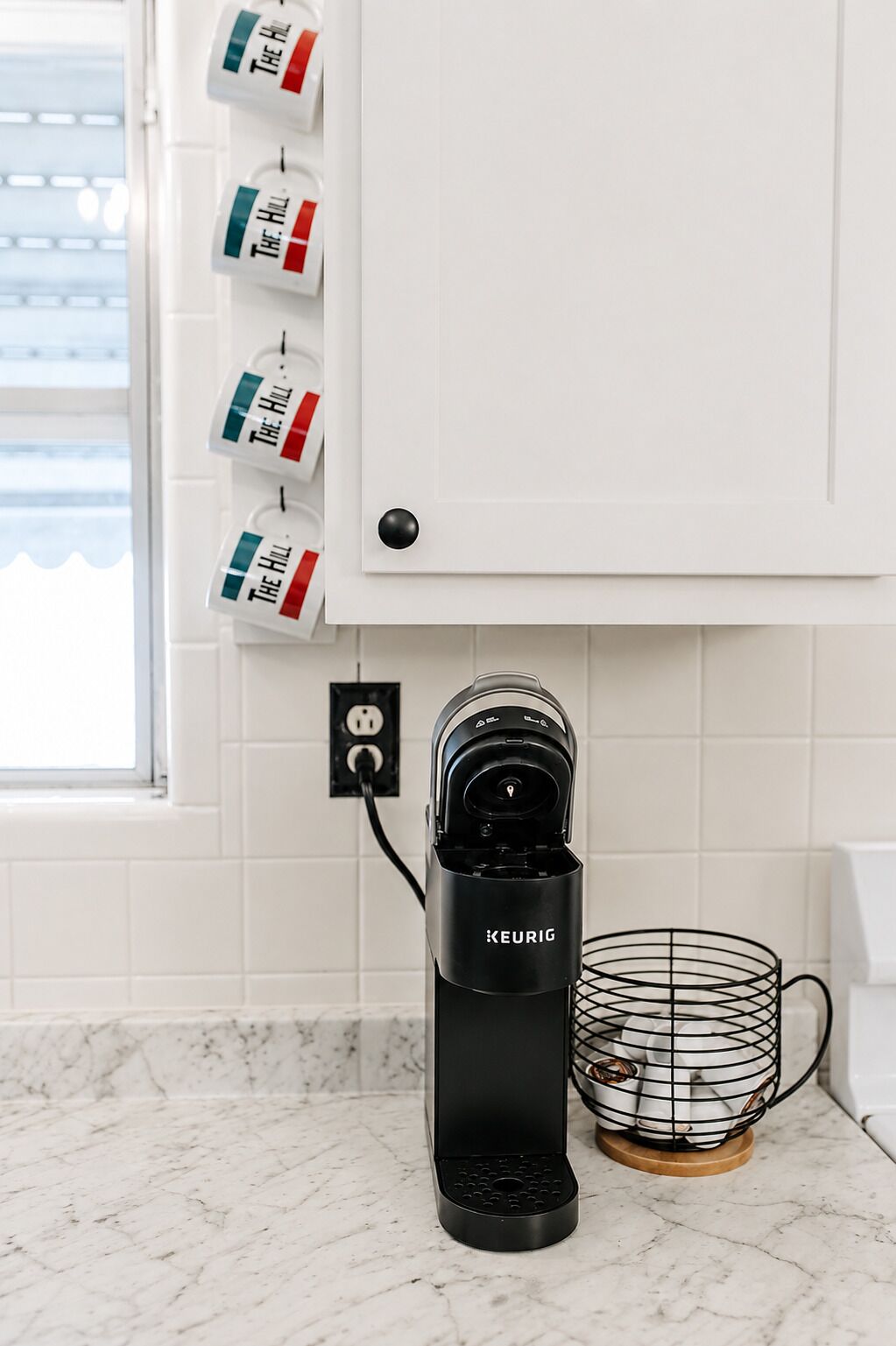 Una cocina con una cafetera Keurig, una máquina de café y un portalápices para cápsulas de café en la pared.