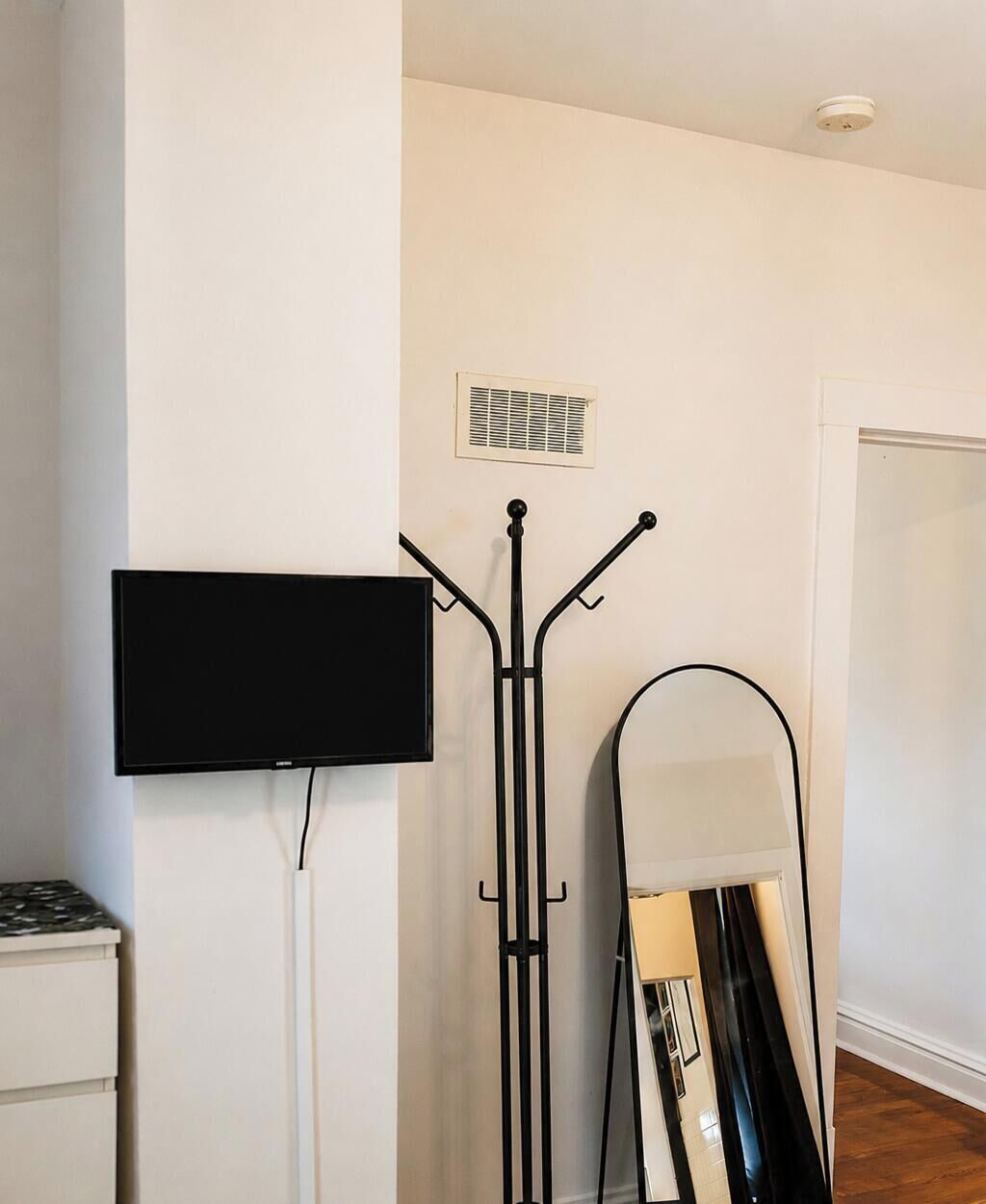 Ein Zimmer mit einem wandmontierten Flachbildfernseher, einem Standventilator und einem Spiegel.