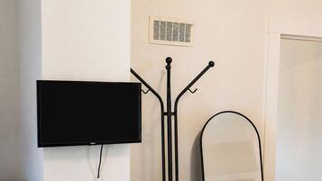 Ein Zimmer mit einem wandmontierten Flachbildfernseher, einem Standventilator und einem Spiegel.