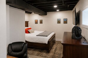 A bedroom with a bed, a desk, a chair, and a fan.