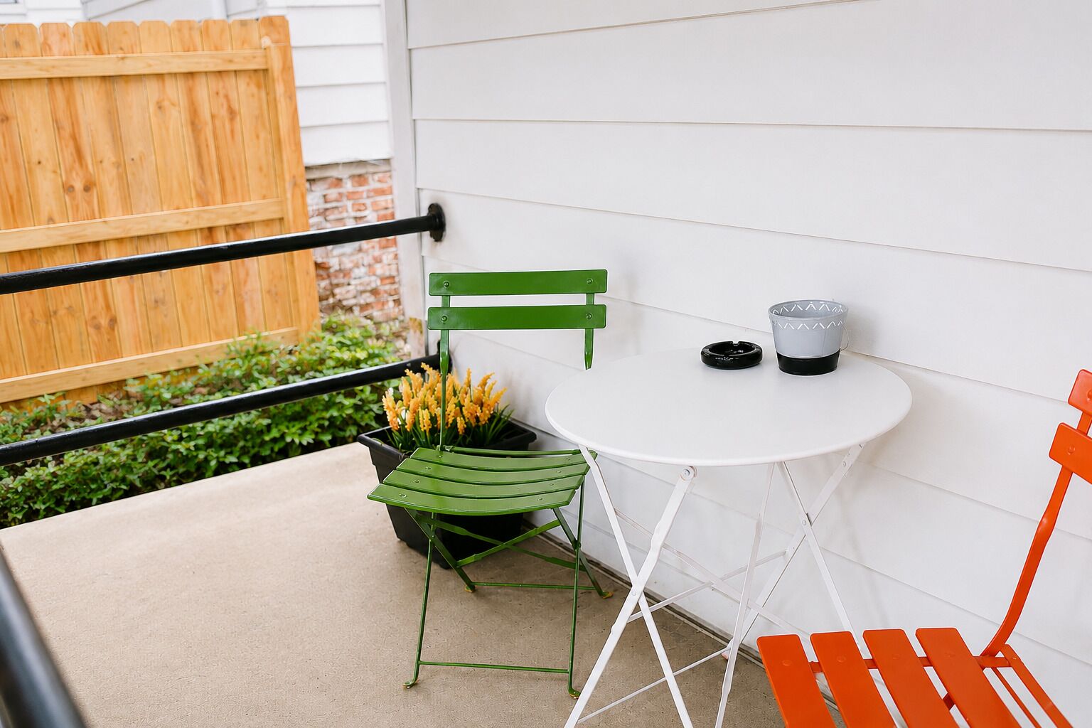 A small outdoor seating area with a white table, a green chair, and an orange chair.