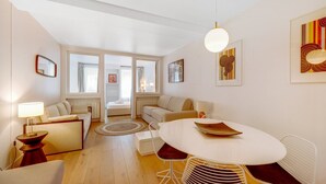 Ein modernes Wohnzimmer mit einem runden Esstisch, einer Couch und einem Bett im Hintergrund.