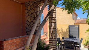 A patio with a stone wall, a tree, and a table with chairs. - Beautiful apartment with small garden (Hyères)