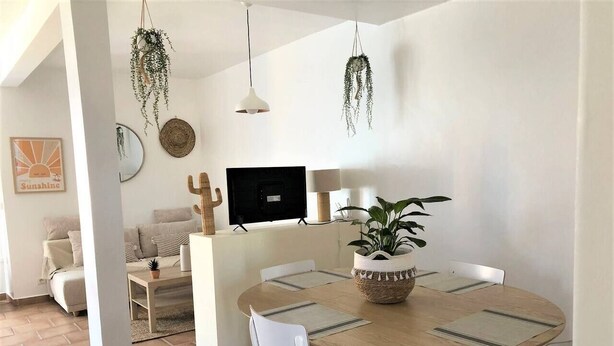 A modern living room with a round wooden dining table, white chairs, a sofa, and a TV. - Beautiful apartment with small garden (Hyères)