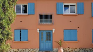 A building with a stone foundation, a blue door, and multiple windows with blue shutters. - Beautiful apartment with small garden (Hyères)