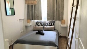 A bedroom with a bed, curtains, a ladder, and a picture on the wall. - Beautiful apartment with small garden (Hyères)