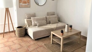A cozy living room with a sofa, a round mirror, a framed artwork, a lamp, and a small table with plants. - Beautiful apartment with small garden (Hyères)