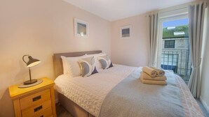 A bedroom with a bed, a bedside lamp, a nightstand, and a window with curtains.