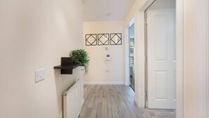 A hallway with light-colored walls, a wooden floor, a black shelf with a plant, and three diamond-shaped wall decorations.