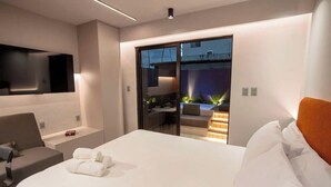 Een moderne hotelkamer met een groot bed, een flatscreen televisie, een sofa en een schuifdeur naar een buitenruimte.