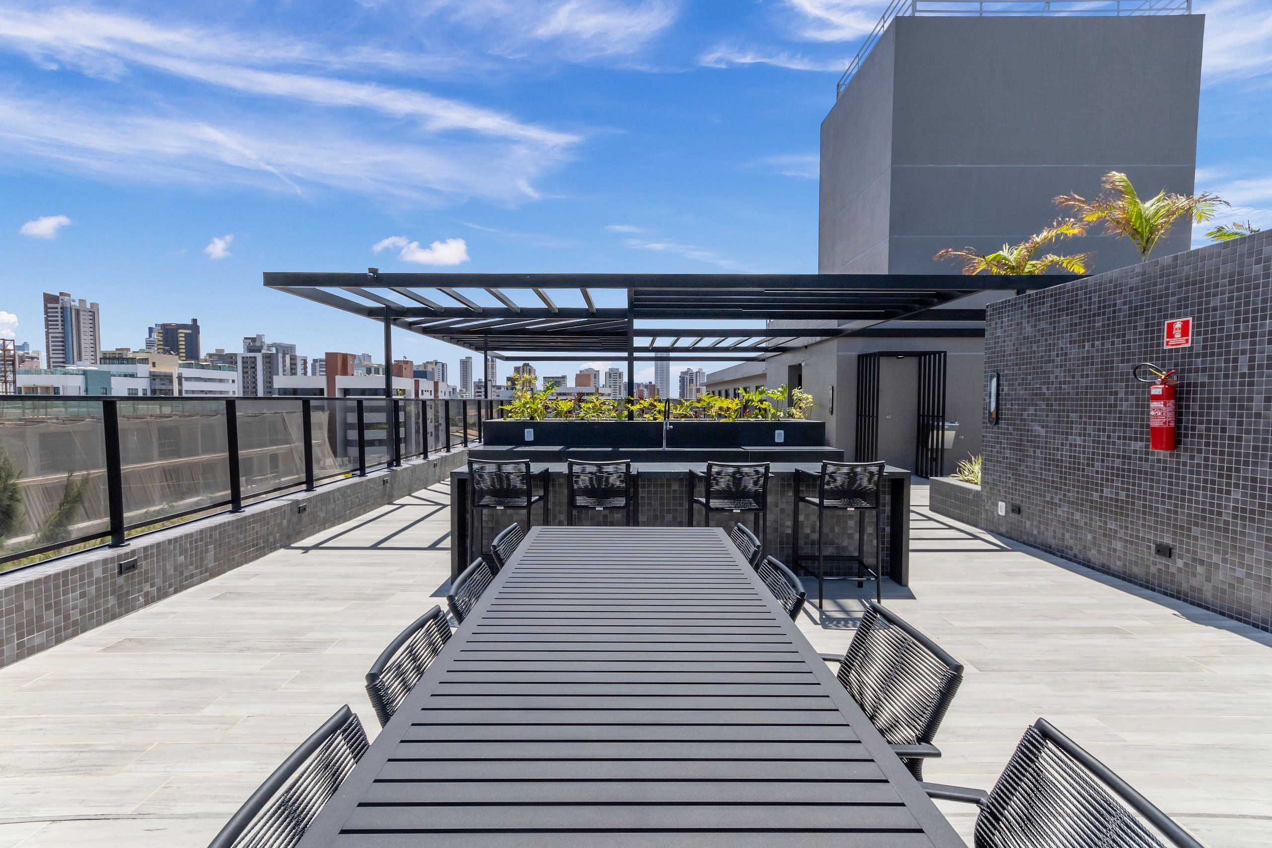 Een terras op het dak met een lange tafel en stoelen, een pergola en uitzicht op de stadshemel.