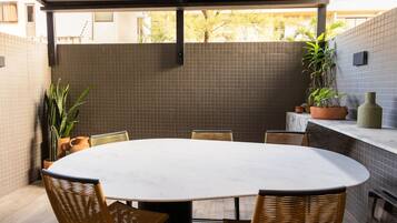 Mesa redonda con sillas, pared de azulejos y plantas en macetas en un espacio exterior cubierto.