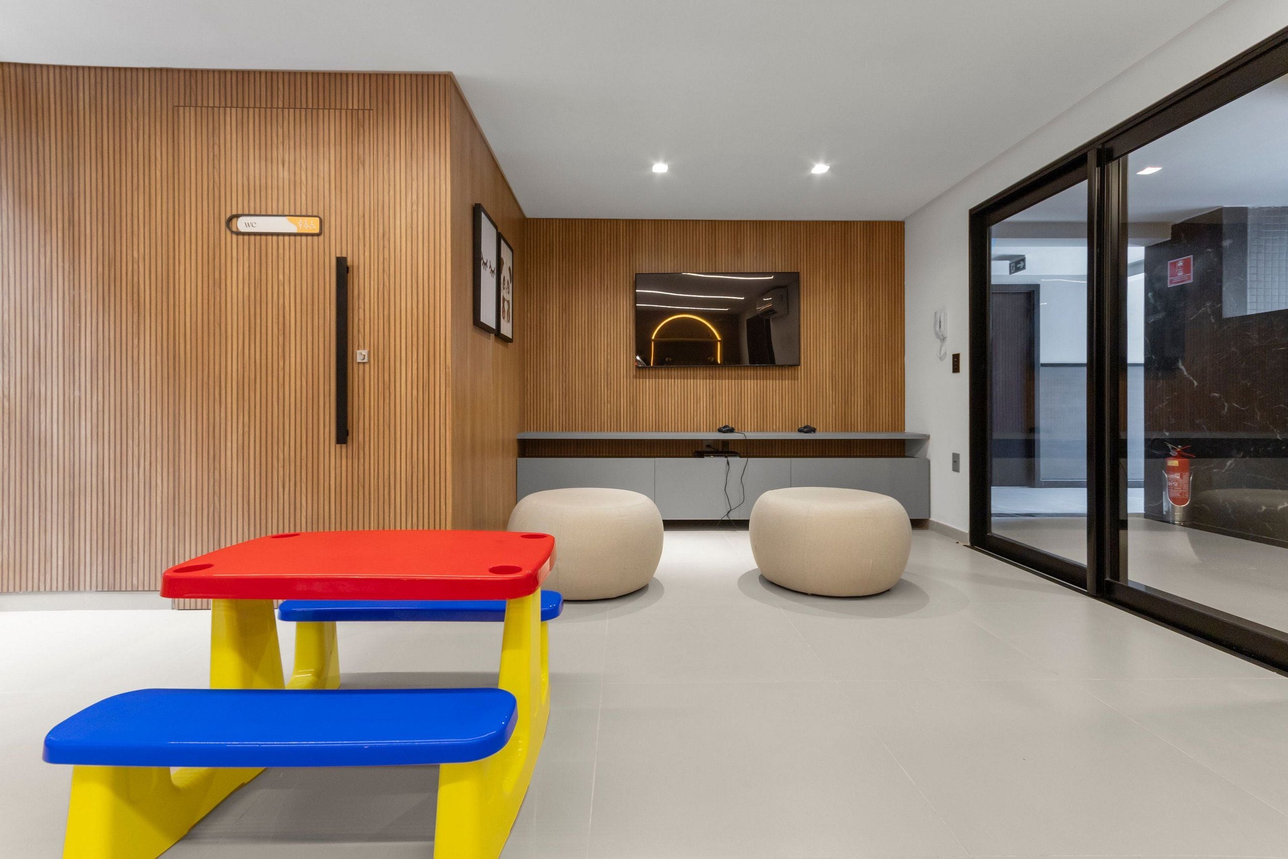 Un interior moderno con una pared de madera, un banco, dos otomanas y un puerta de vidrio.
