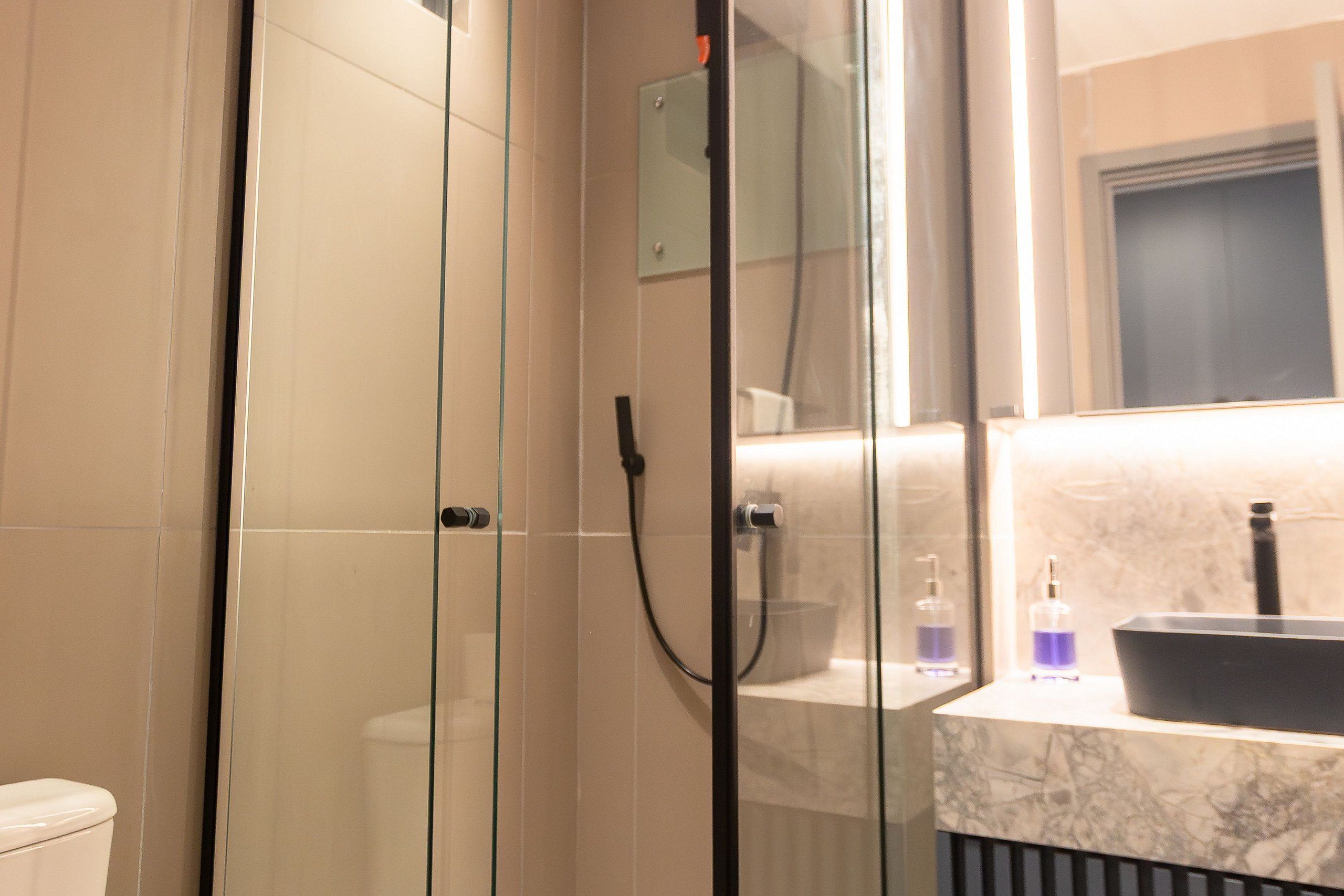 A bathroom with a glass-enclosed shower, a toilet, and a sink with a marble countertop.