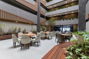 Een meerlaagse binnenruimte met meerdere eettafels en stoelen, houten leuningen en potplanten.