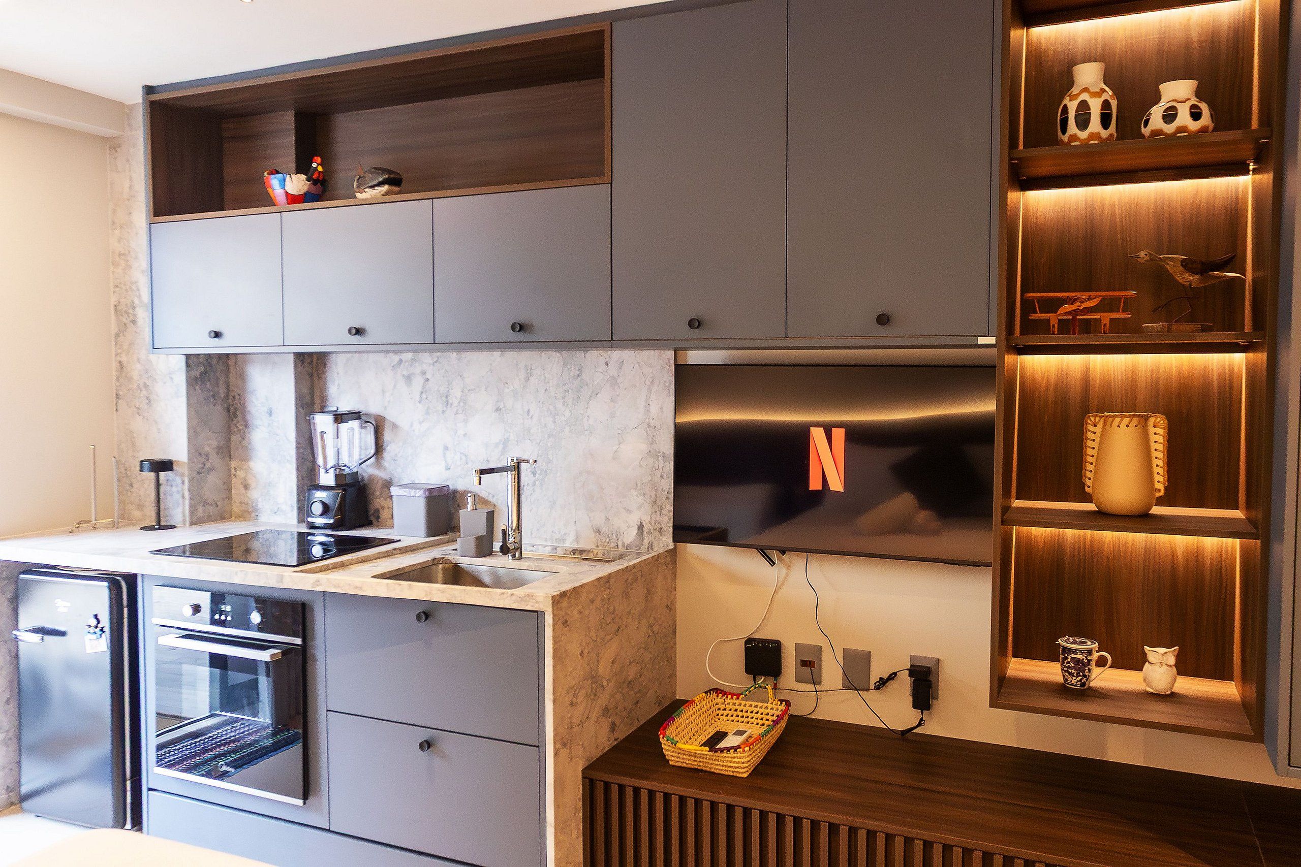 Una cocina moderna con electrodomésticos integrados, encimera de mármol y estanterías de madera con objetos decorativos.