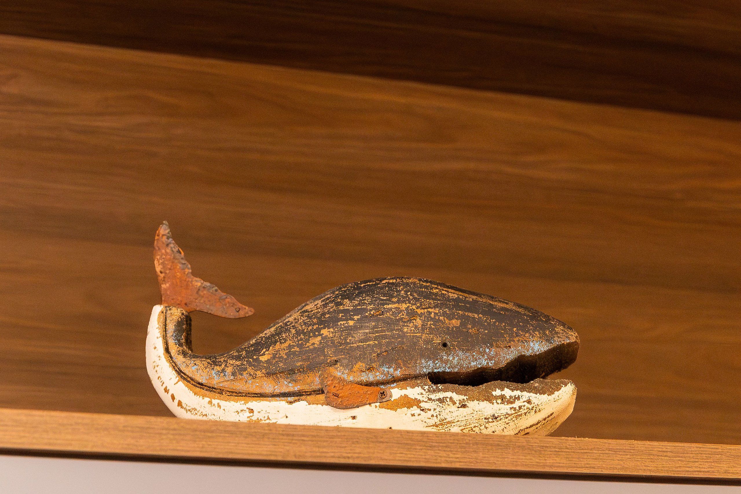 A rustic, weathered wooden shelf with a single, aged, metal object resembling a fish.