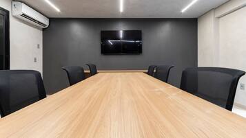 Uma sala de conferências com uma longa mesa de madeira, quatro cadeiras pretas, uma TV de tela plana na parede e um aparelho de ar condicionado à esquerda.