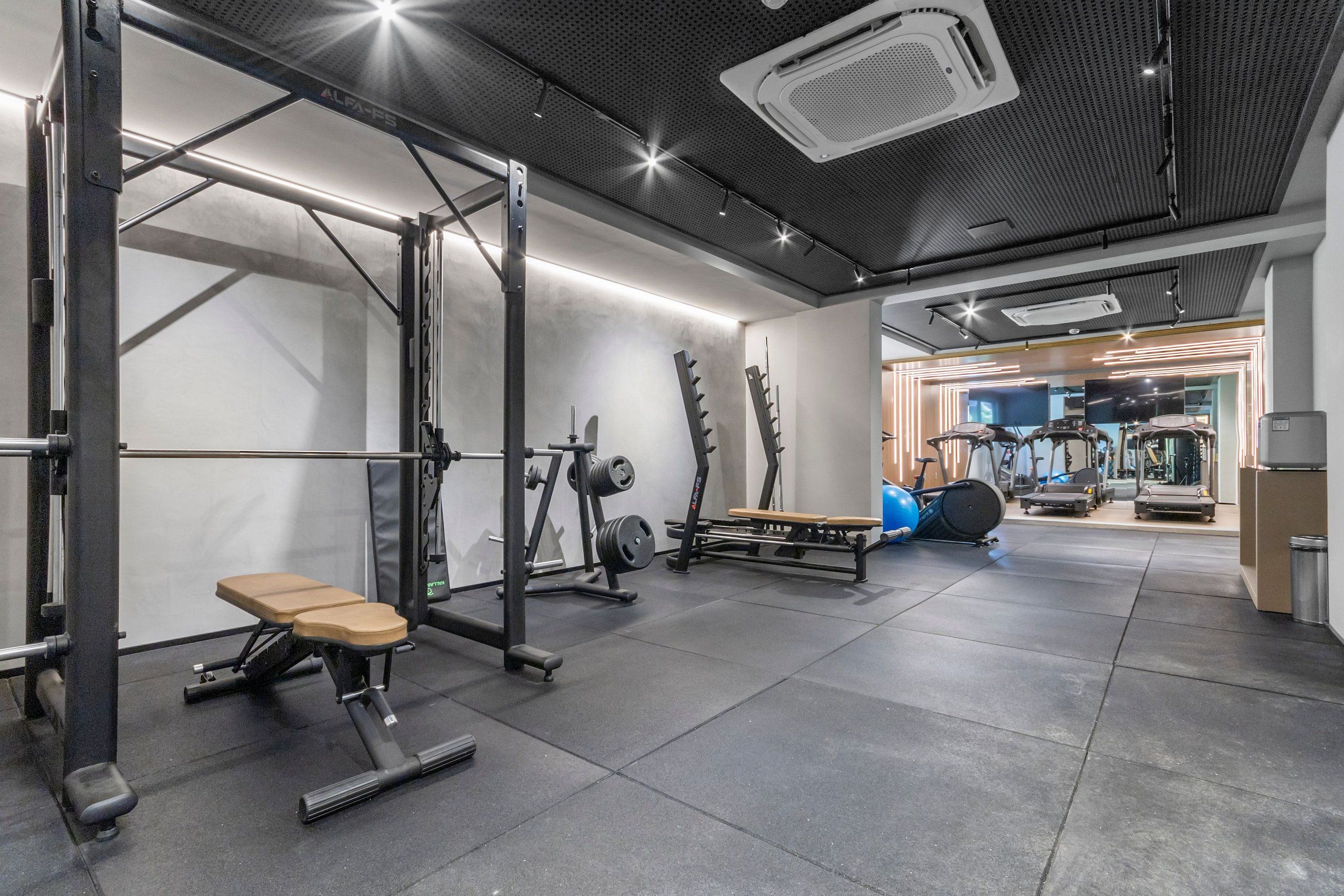 Uma academia com equipamentos de musculação, um banco e um espelho grande na parede.