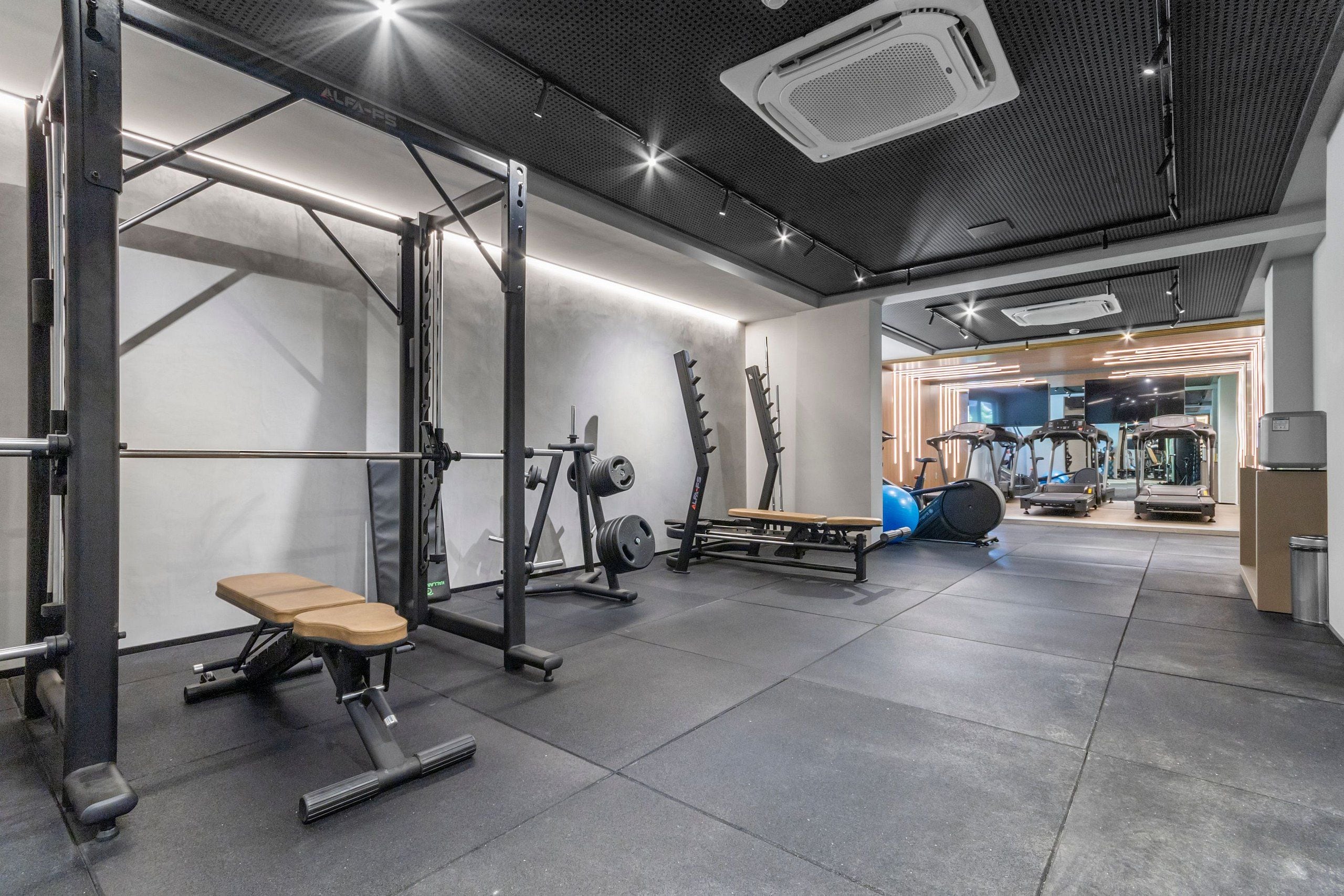 A gym with weightlifting equipment, a bench, and a mirrored wall.