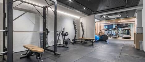 A gym with weightlifting equipment, a bench, and a mirrored wall.