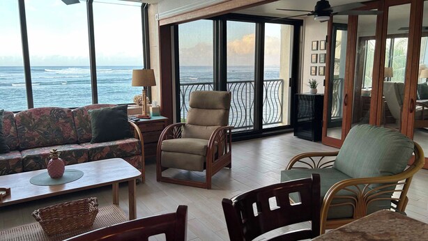 Een ruim balkon met uitzicht op de oceaan, voorzien van een bank, stoelen en een tafel.