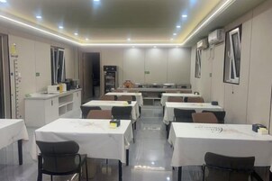 Un comedor con mesas y sillas, una cocina al fondo e iluminación empotrada en el techo.