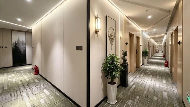A hotel hallway with a patterned floor, wall-mounted light fixtures, and a potted plant. - GreenTree Inn Express Hotel (Beijing Fangshan District Government Longhu Tianjie) (Beijing)