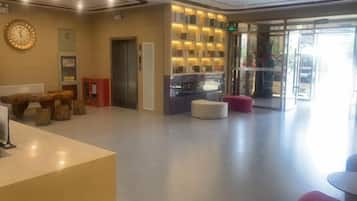 A hotel lobby with a reception desk, seating area, and a glass door entrance.