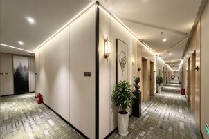 Un pasillo de hotel con piso estampado, luminarias empotradas en la pared y una planta en maceta.