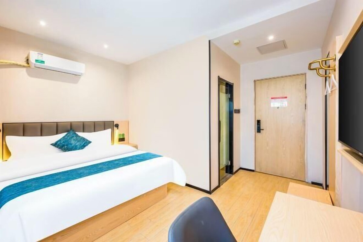 A hotel room with a bed, bedside table, chair, and a door.
