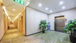 A hotel corridor with a patterned floor, a reception desk, an elevator, and potted plants. - GreenTree Inn Express Hotel (Beijing Fangshan District Government Longhu Tianjie) (Beijing)