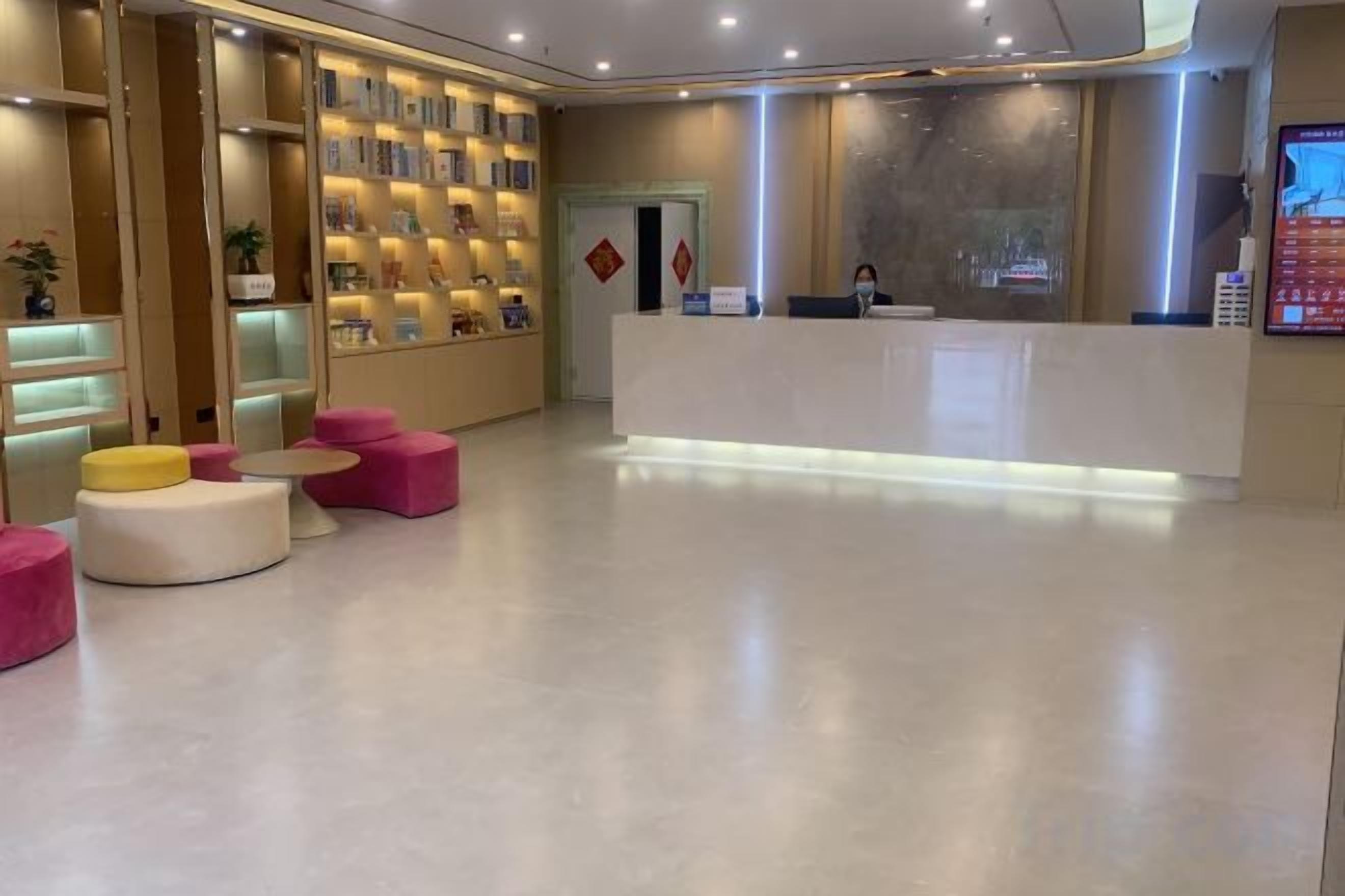 Un vestíbulo de hotel con mostrador de recepción, zona de estar con mesas y sillas redondas, y una pared con estantes que exhiben objetos.
