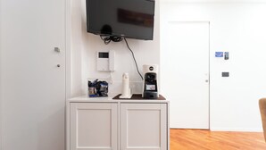 Ein Zimmer mit an der Wand montiertem Fernseher, einer Kaffeemaschine und einem Spender in einem Schrank.