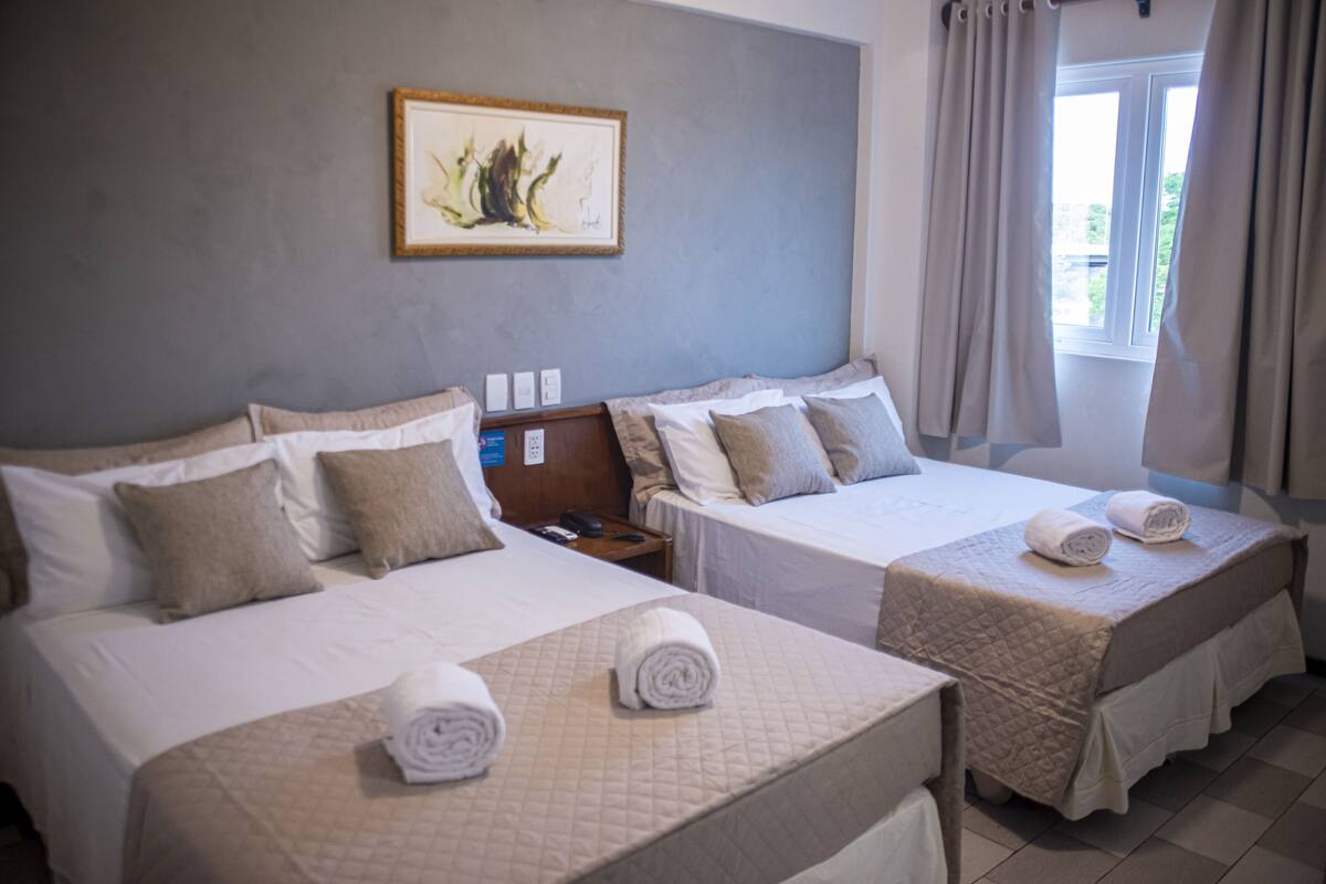 A hotel room with two beds, each with a quilted bedspread and pillows, a nightstand with a phone, and a framed artwork on the wall.