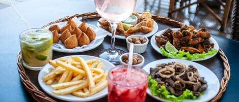 A table with a variety of food items including croissants, fries, and grilled meat, along with drinks and a glass of pink beverage.